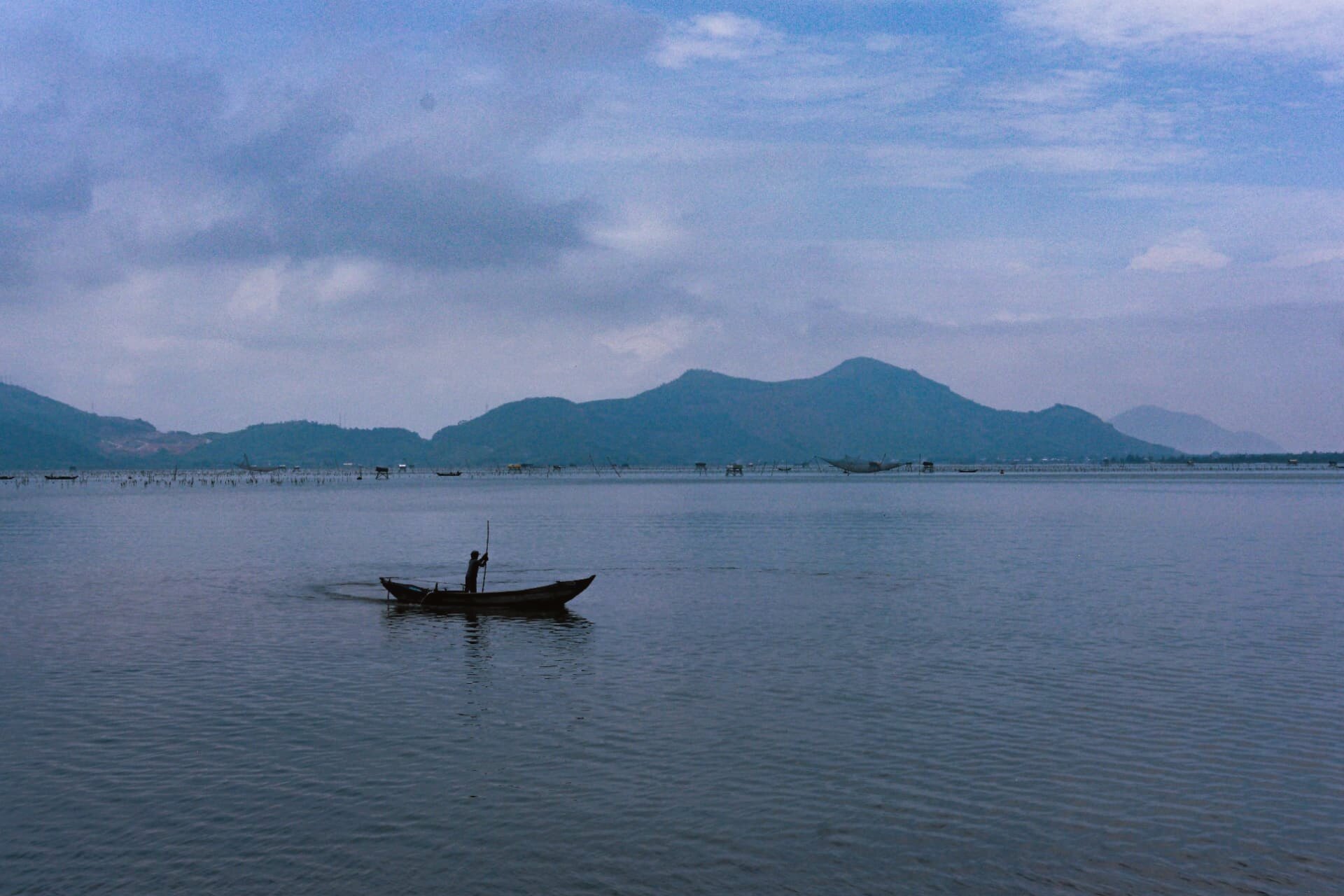 Fisherman poling a wooden boat across a calm lagoon at first light